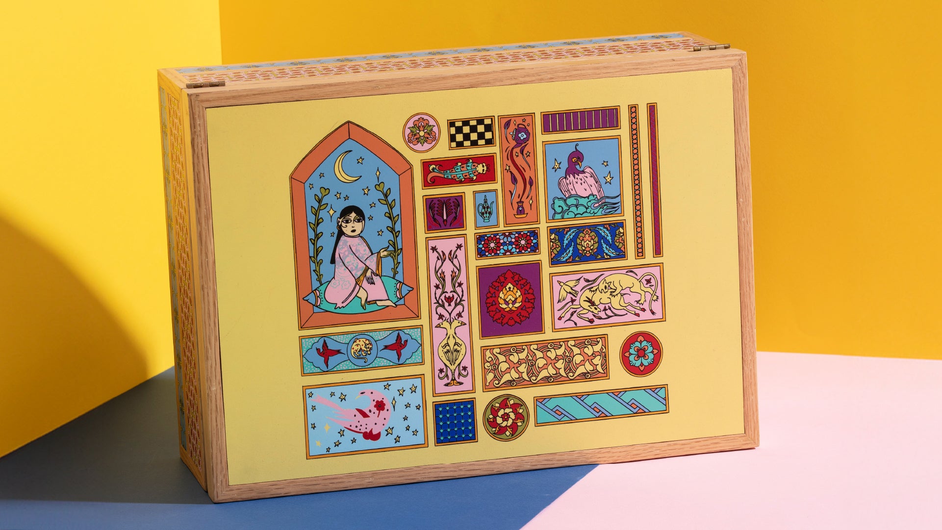 View of the colorful and intricate wooden set that comes with the teaset. Arabic inspired drawing on the front. Pink, blue and yellow background