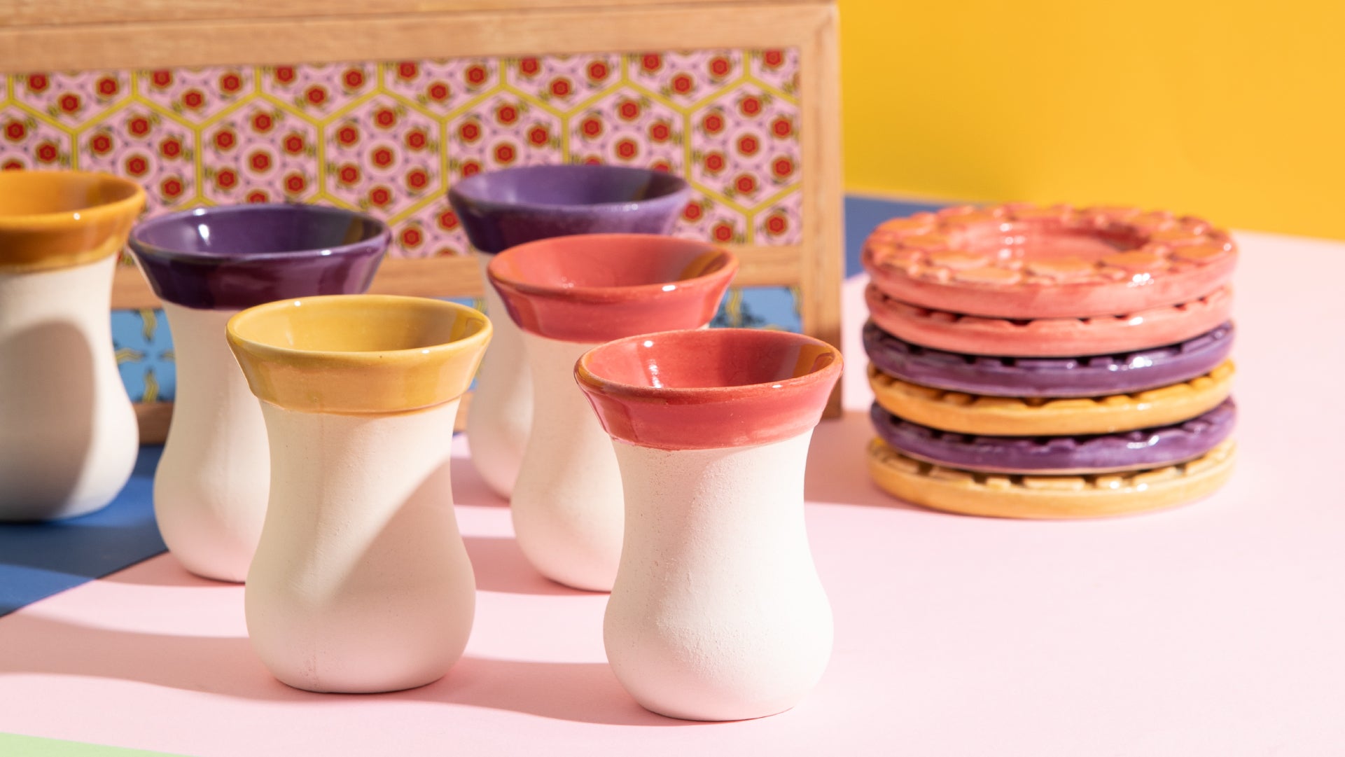Overview of lots of differently colored cups and they corresponding coaster. Blurred view of the container in the backgroun